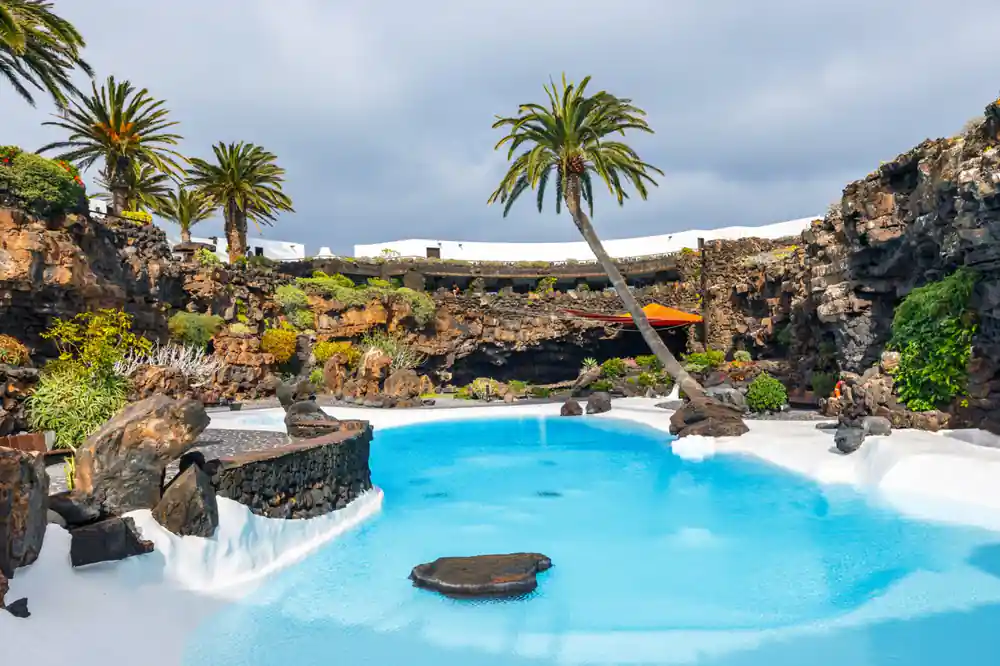 Bright blue mineral pool with rock formations and palms