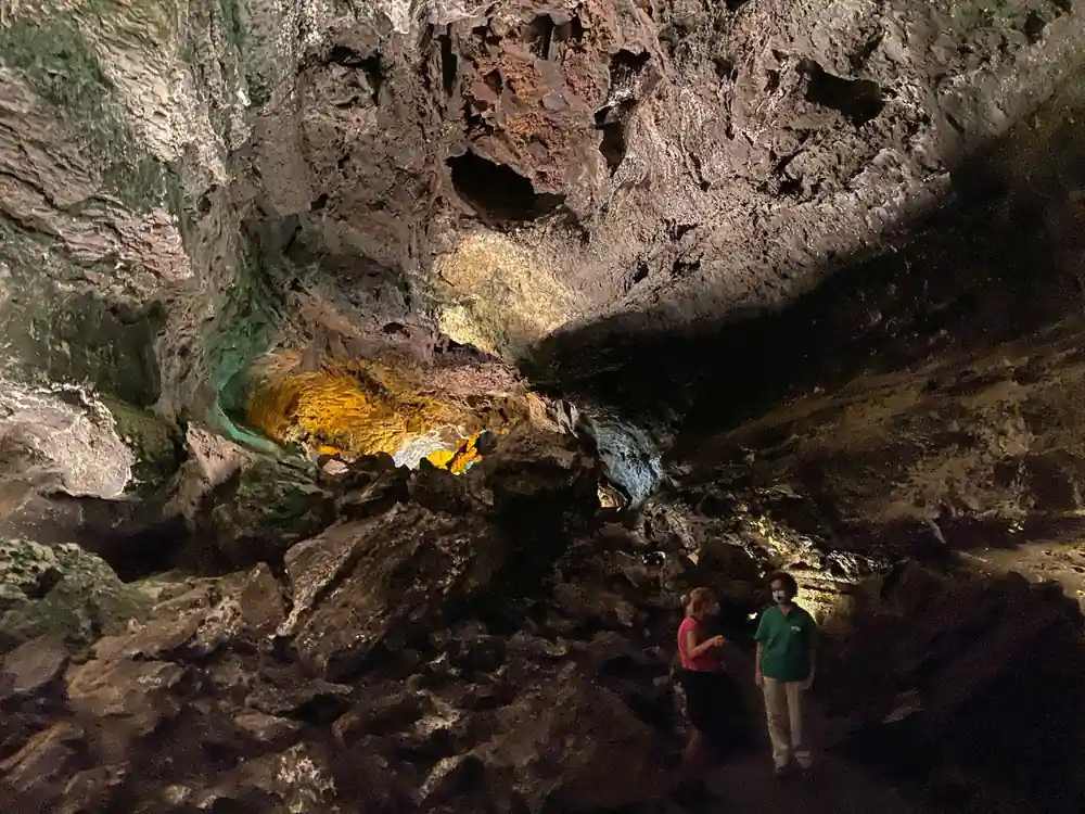 Cave interior with yellow mineral deposits and two visitors