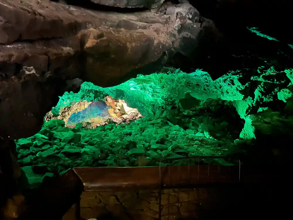 Cave opening over deep turquoise water with green-lit rock