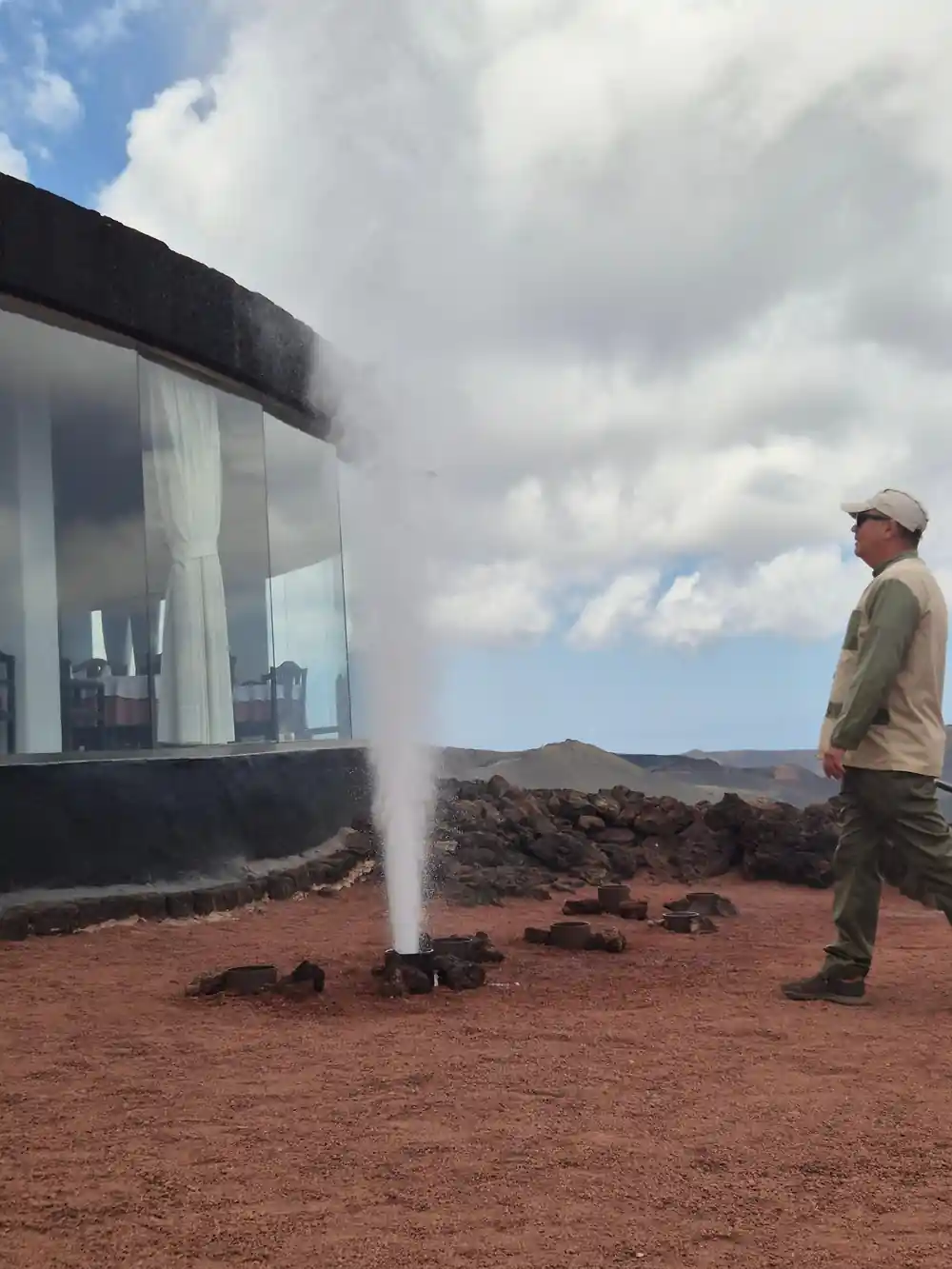 Geothermal geyser erupting near modern building and observer