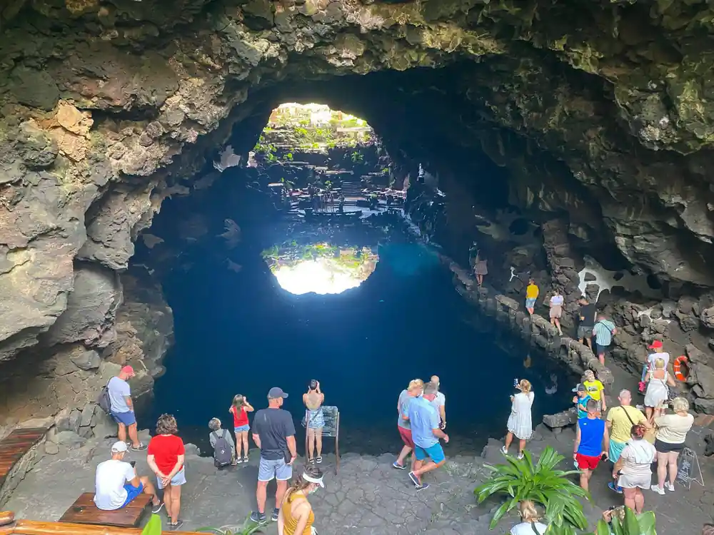 Large cave opening with bright blue water and crowd of tourists