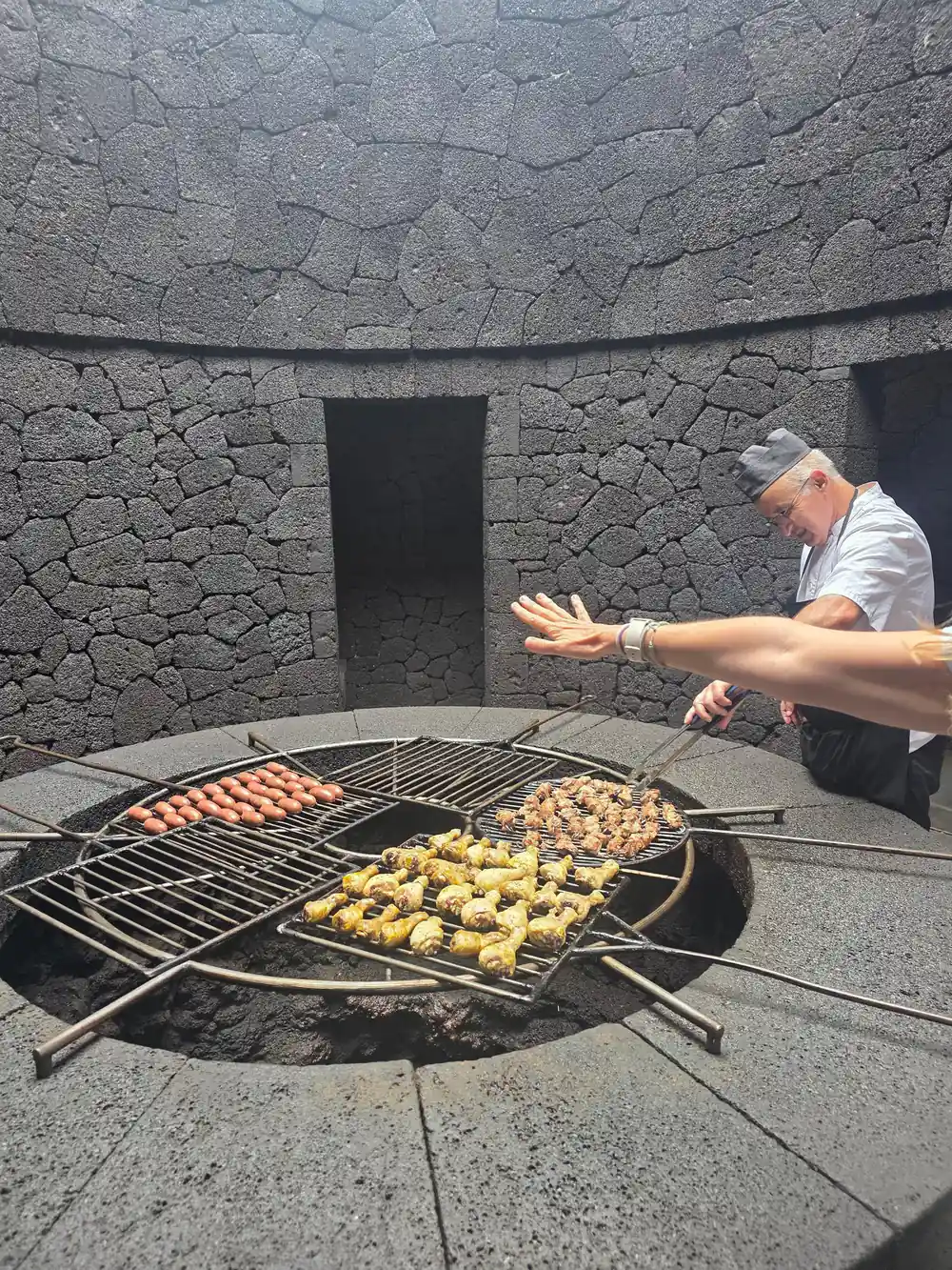 Man cooking food on outdoor fire pit with lava stone structure