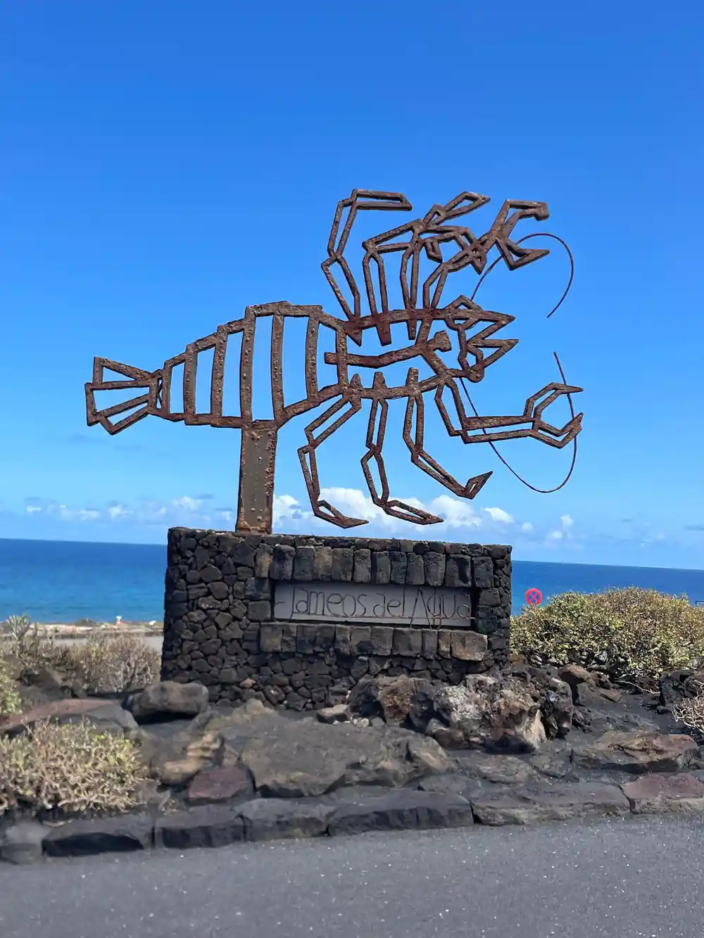 Metal scorpion sculpture on black stone base with ocean background