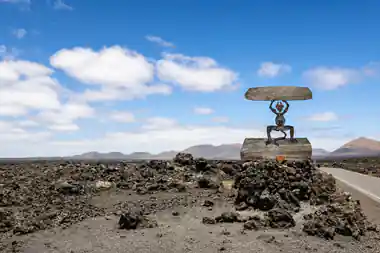 Metal sculpture of figure holding disk on lava field