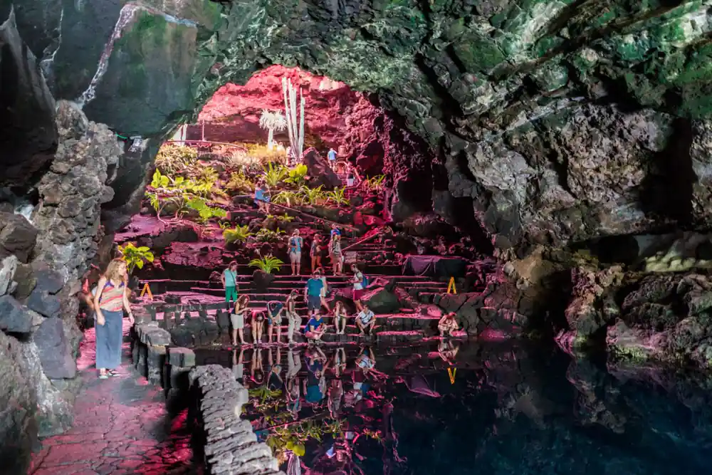 Pink algae-filled pool in cave with tourists visible