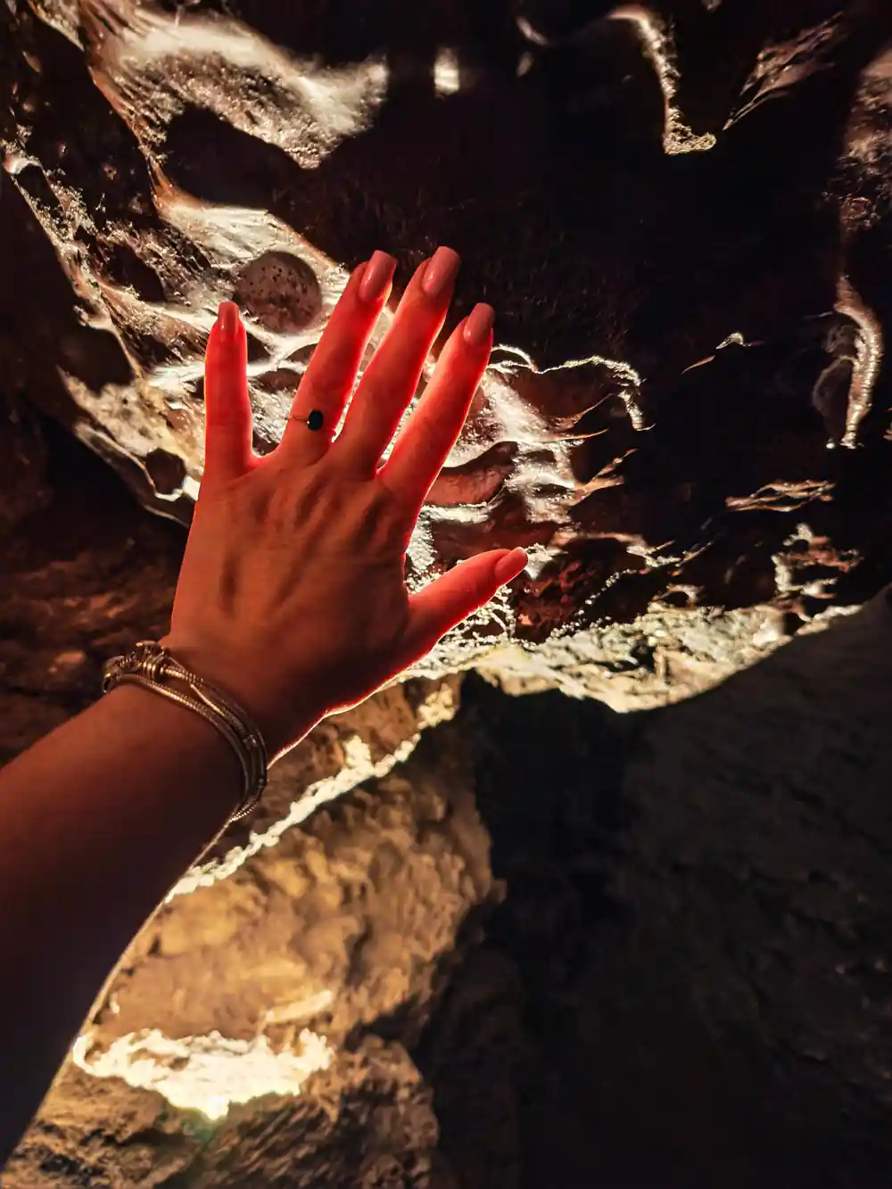 Red hand touching bright mineral formations in cave opening