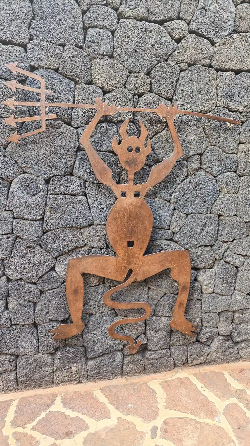 Rust metal figure sculpture mounted on grey stone wall