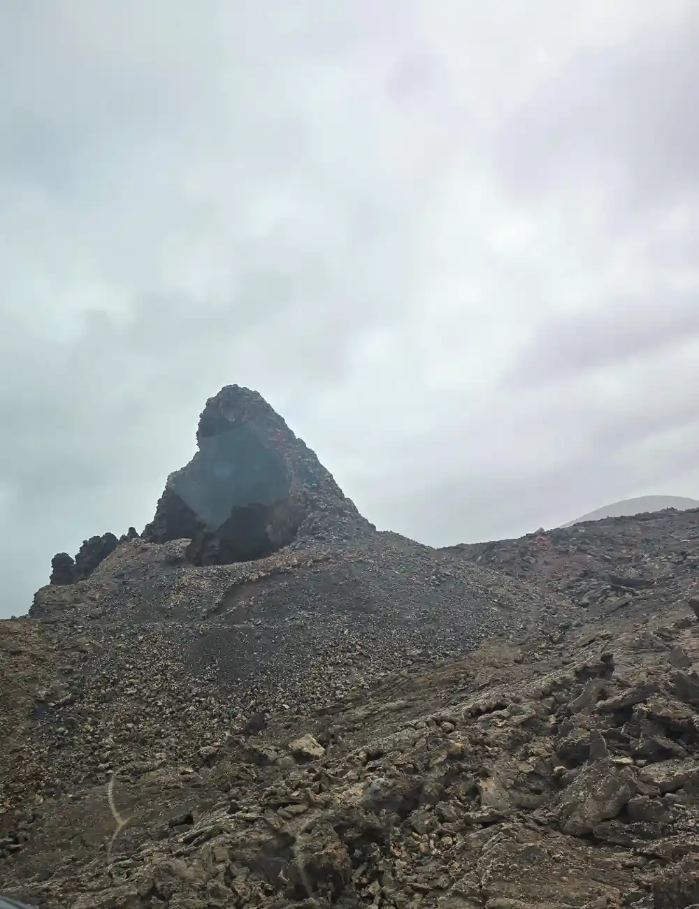 Steep rocky volcanic peak on barren grey terrain