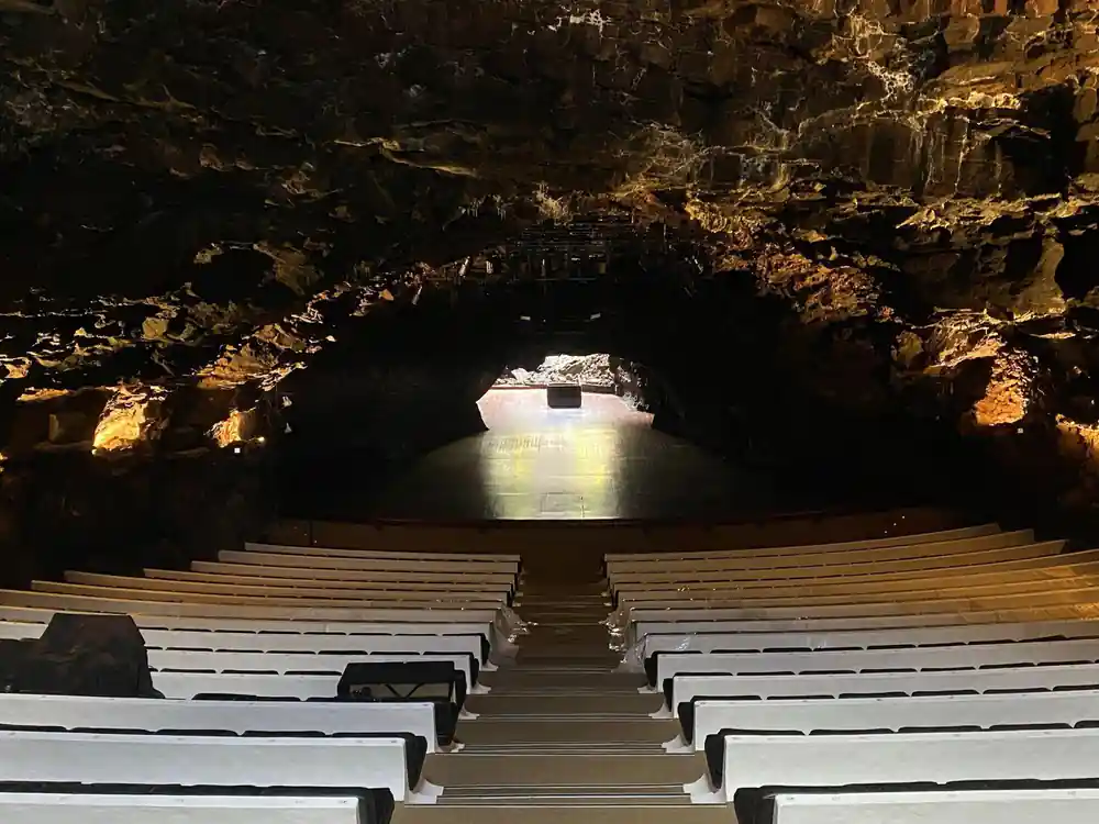 Underground cave chamber with wooden seating facing illuminated opening
